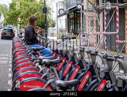 Santander Fahrradstation voll beladen, mit einer Frau, die ein Fahrrad als Sitz benutzt, während sie in London telefoniert Stockfoto