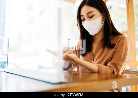 Junge schöne asiatische Frau trägt covid-19 Schutz Gesichtsmaske Anwendung Medizinisches Händedesinfektionsmittel für Sicherheit und Vorsorge gegen Coronavirus-Viren Stockfoto