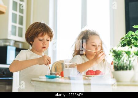 Zwei Geschwister Bruder und Schwester Kleinkind junge Tween Mädchen Malerei ostereier in der Küche zu Hause am sonnigen Frühlingstag Stockfoto