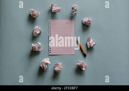 Ein leeres Blatt Papier, ein alter Bleistift, umgeben von Resten zerknitterter Papierkugeln auf hellblauem Hintergrund mit Schatten. Die Seite ist aus einem Frühling-lo gerissen Stockfoto