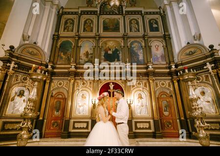 Der Bräutigam und die Braut in den Kränzen stehen die Hände haltend Am Altar der Kirche während der Hochzeit Stockfoto