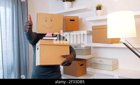 Daumen hoch. Unkenntlich Mann mit Karton-Box über dem Kopf Paket Bücher und Sparschwein Umzug in neue Eigenschaft. Investieren in Immobilien-Konzept. Hochwertige Fotos Stockfoto