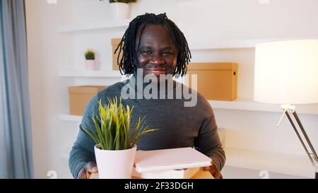 Aufgeregt junger afroamerikanischer Mann zieht in die neue Wohnung. Halten von Kartons mit Pflanzen und Büchern. Hochwertige Fotos Stockfoto