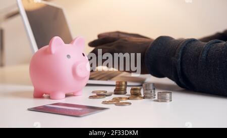 Hände von schwarzen Mann arbeiten auf dem Laptop hinter Sparschwein und Münzen. Buchhaltungs- und Finanzkonzept. Hochwertige Fotos Stockfoto
