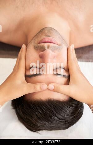 Professionelle Masseurin macht Kopf- und Gesichtsmassage im Wellnesscenter. Mann bekommt Gesichtsstraffung Massage im Spa Salon Stockfoto
