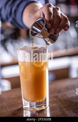 Hand eines Barkeepers, der eine Flüssigkeit in den Cocktail mit Schaum auf der Oberseite gießt. Stockfoto