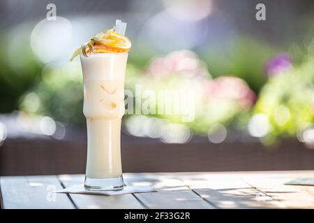 Pinacolada oder Milkshake Cocktail mit Strohhalmen und Orange auf der Oberseite serviert in einem hohen Glas auf einer Sommerterrasse. Stockfoto