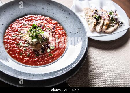 Rote Tomatensuppe serviert auf einem Teller mit Gemüse und Käse auf der Oberseite neben Scheiben Brot. Stockfoto