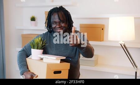 Daumen hoch. Unkenntlich Mann mit Karton-Box über dem Kopf Paket Bücher und Sparschwein Umzug in neue Eigenschaft. Investieren in Immobilien-Konzept. Hochwertige Fotos Stockfoto