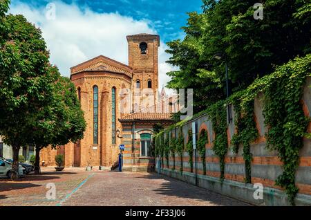 Blick auf die enge Kopfsteinpflasterstraße und die katholische Backsteinkirche in der Altstadt von Alba, Piemont, Norditalien. Stockfoto