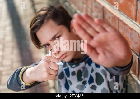 Ein kaukasischer Teenager hält eine zerbrochene Zigarette in der Hand und zeigt ein Stoppschild, das gegen das Rauchen protestiert. Das Konzept der Jugendlichen Rauchen addi Stockfoto