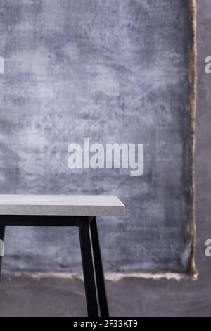 Tisch oder Metall Hocker und abstrakt bemalte Leinwand in der Nähe Betonwand Hintergrund. Tischplatte oder Ablage Stockfoto