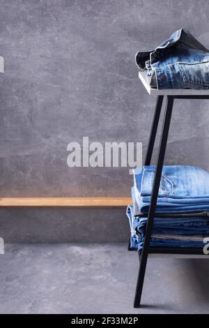 Denim Jeans am Stuhl oder Regal der Rack in der Nähe graue Wand Hintergrundstruktur. Vorderansicht der klassischen Jeans-Mode Stockfoto