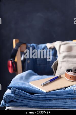 Stapel von Denim Jeans an alten Holzstuhl in der Nähe dunkelschwarzen Wand Hintergrund Textur. Moderner Casual-Style der klassischen Jeans-Mode Stockfoto