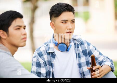 Junge asiatische Männer trinken Bier, während sie gemeinsam im Freien Zeit verbringen Stockfoto