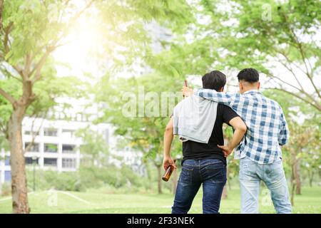 Rückansicht von zwei jungen Freunden, die mit Bier und stehen Reden im Freien Stockfoto