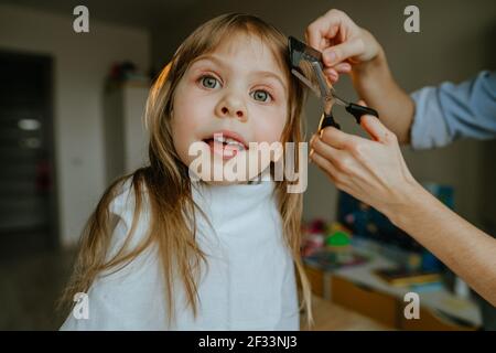 Nahaufnahme der Hände der weiblichen Mutter, die Haare ihrer vier Jahre alten Tochter zu Hause im Kinderzimmer schneiden. Tägliche Routine zu Hause. Stockfoto