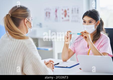 Arzt in Maske erklärt Diagnose zu ihrer weiblichen Patientin Stockfoto