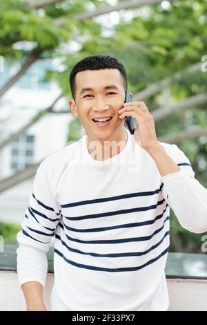Asiatische junge Mann Blick auf Kamera während im Gespräch auf Handy Telefon in der Stadt im Freien Stockfoto