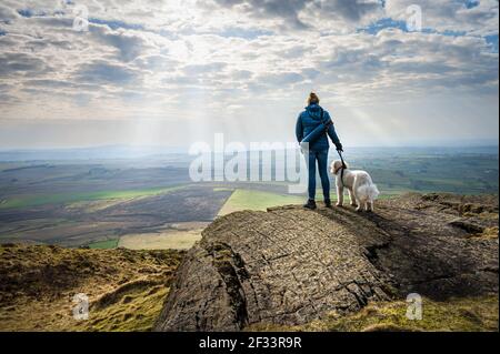 Eine Frau und ihr weißer Hund genießen die Aussicht auf Die irische Landschaft nach dem Klettern auf dem Slemish Mountain in Nordirland Stockfoto