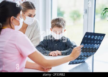 Arzt diskutiert Röntgenergebnisse mit Mama und ihrem Sohn alle Masken tragen Stockfoto