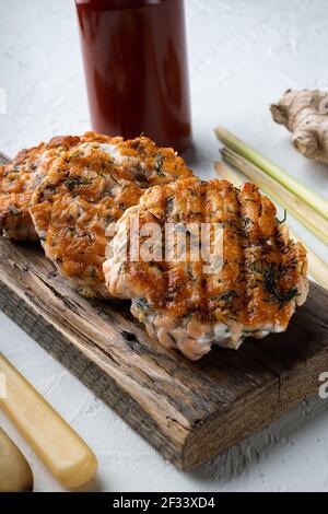 Gegrillte schnelle asiatische Fischkuchen aus Lachs und würzigen Kraut, auf weißem strukturierten Hintergrund Stockfoto