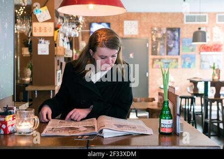 Breda, Niederlande. Mid adutl kaukasische Frau beim Lesen einer Zeitung, während Sie eine Bar besuchen. Stockfoto