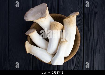 Pilze eringi in der braunen Schale auf dem schwarzen Holzhintergrund.Draufsicht.Nahaufnahme. Stockfoto