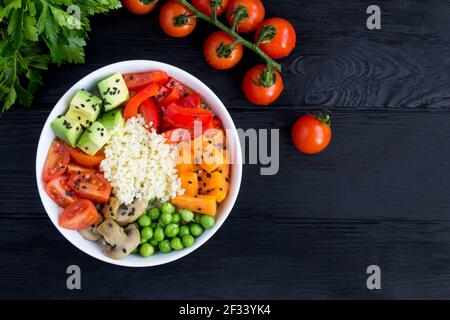 Vegane Poke Schale mit Couscous und Gemüse in der weißen Schale auf dem schwarzen Holzhintergrund. Draufsicht. Speicherplatz kopieren. Nahaufnahme. Stockfoto