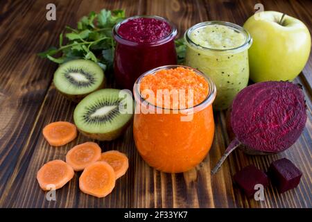 Verschiedene Gemüse- und Obstsmoothies oder Püree in den kleinen Gläsern auf dem braunen Holzhintergrund. Nahaufnahme. Stockfoto