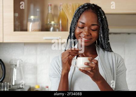 Porträt von glücklich lächelnd junge schwarze Frau Mischen Milch und Zucker in einer Tasse Kaffee am Morgen Stockfoto