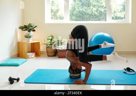 Fit starke junge Schwarze Frau üben Kopfstand Pose auf dem Boden Morgens im Zimmer Stockfoto