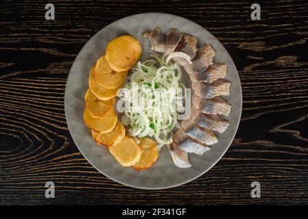 Hering in Scheiben mit Zwiebeln und gebackenen Kartoffeln auf einem grauen Teller auf einem dunklen Holztisch. Draufsicht. Stockfoto