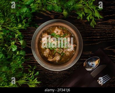 Suppe mit Fleisch, Sauerampfer und Kräutern auf einem Hintergrund von Petersilienzweigen auf einem dunklen Holztisch. Wunderschöne Tischeinstellung. Stockfoto