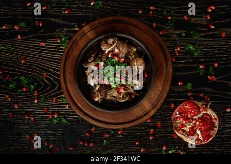 Grillen Sie Fleisch mit Zwiebeln in einem Tonteller auf einem Holzbrett auf einem dunklen Holztisch, der mit Granatapfel und Koriander verziert ist. Wunderschöne Tischeinstellung. Stockfoto