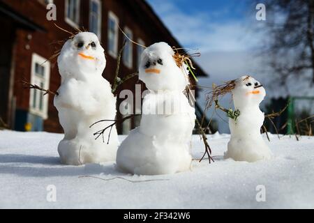 Winter-Frühling Geschichte der Schneemann Familie Schneemann-Vater, Schneemann-Mutter, Schneemann-Kind im Schnee vor dem Hintergrund eines Dorfhauses Stockfoto