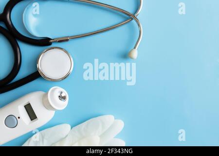 Behandlungskonzept der Medizin. Elektronisches Thermometer, Phonendoskop oder Stethoskop, weiße Handschuhe auf blauem Hintergrund. Hochwertige Fotos Stockfoto