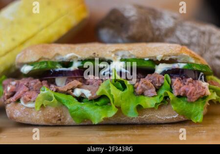 Thunfisch-Sandwich mit roten Zwiebeln, Salladen und Gurkenscheiben, die sich auf einem Holztisch bewegen Stockfoto