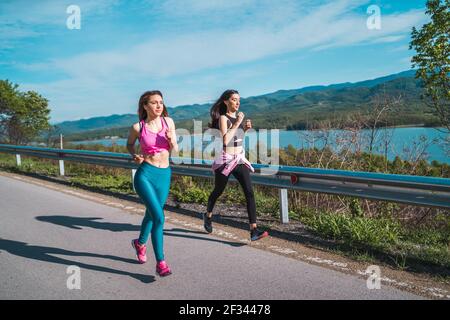 Zwei weibliche Sportmodelle laufen auf Asphaltstraße in der Nähe des Sees Im Freien Stockfoto