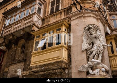 Traditionelle maltesische Häuser mit hölzernen überdachten Balkonen und St. Michael Der Erzengel besiegt die Teufelsstatue an der Gebäudeecke Stadt Valle Stockfoto