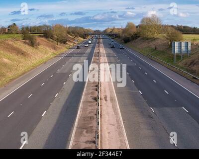 Leichter Verkehr auf einem geraden Abschnitt der Autobahn in Großbritannien an einem sonnigen Tag im Winter. Reparaturen an der Fahrbahn sind im Vordergrund zu sehen. Stockfoto