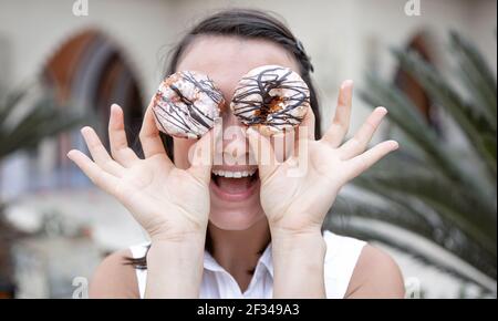 Lustige Mädchen posiert mit Donuts im Sommer draußen. Urlaubs- und Urlaubskonzept. Stockfoto