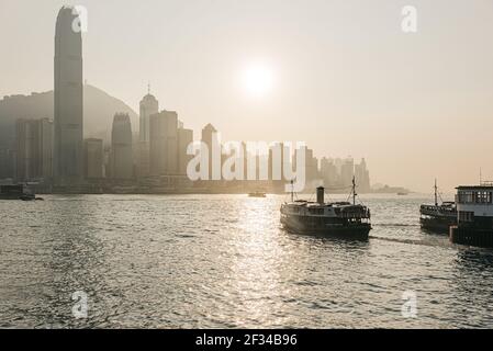 Der Blick von Kowloons Tsimshatsui Kai über Victoria Hafen zu Hong Kong Island als Star Ferry geht es quer durch Das Wasser Stockfoto