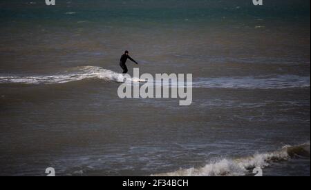 Ein lokaler Surfer am Strand von West Wittering hält sich in sozialer Distanz, da der Parkplatz geschlossen werden muss, nachdem am Samstag Tausende von Menschen auftauchten. Stockfoto