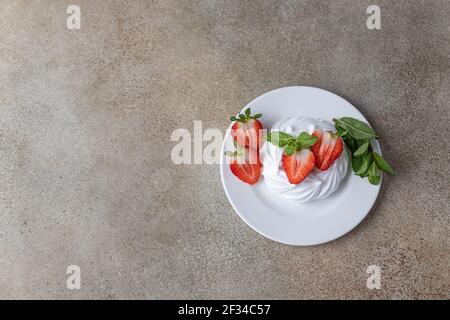 Mini Pavlova Meringue Kuchen mit Erdbeeren und Minze auf einem Teller, Beton Hintergrund. Draufsicht. Selektiver Fokus. Stockfoto