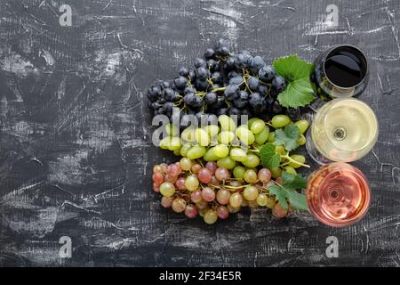 Sortiment verschiedene Arten von Wein und Traubensorten. Weißer Rosé-Rotwein in Weingläsern in der Nähe von weißen rosa und schwarzen Trauben. Tafelwein im Dunkeln Stockfoto