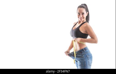 Fit gut aussehende Frau zeigt großen Gewichtsverlust durch lose Jeans tragen Sport-BH auf einem isolierten weißen Hintergrund. Stockfoto