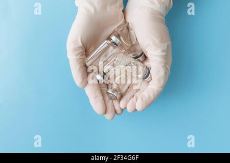 Medizin Behandlung, Impfkonzept. Arzt Hände in weißen Handschuhen hält Flaschen mit Impfstoff, Antibiotika oder andere Medikamente auf blauem Hintergrund Stockfoto