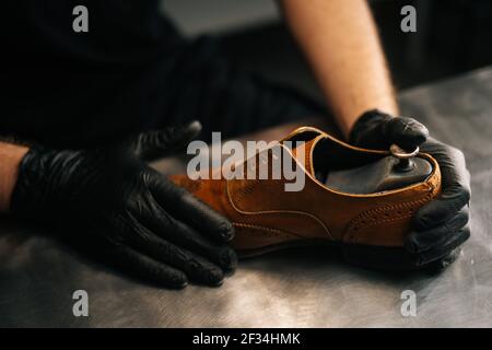 Nahaufnahme der Hände eines schwarz getragenem Schuhmacherschuhrers von oben Handschuhe fügen in abgenutztes hellbraunes Leder eine Schuhunterlage aus Holz ein Schuhe Stockfoto