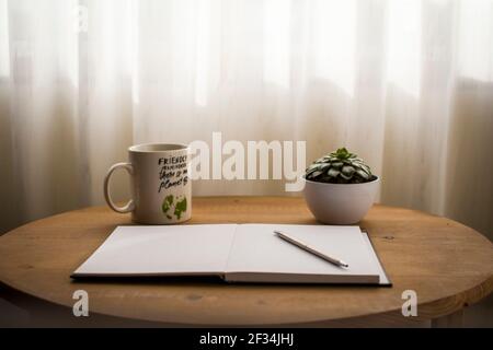Minimalistischer Arbeitsplatz zu Hause, mit einer Tasse Kaffee und einem offenen, leeren Notizbuch auf dem Schreibtisch Stockfoto
